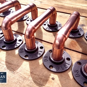 May include: Close-up of several copper pipe handles with black iron flanges. The handles are arranged in a row on a wooden surface. Each handle has a black iron flange with the text "DS" and a number.