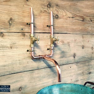 Può includere: Rubinetto per lavabo da parete in rame con due valvole in ottone e un becco in rame. Il rubinetto è montato su una parete in legno e il lavabo è una ciotola in rame.