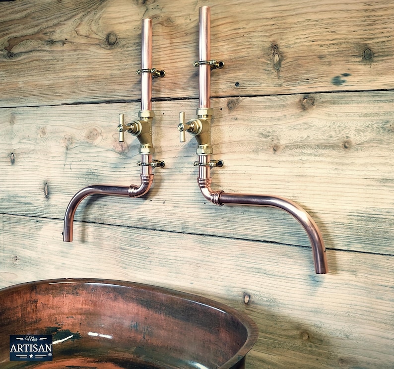 May include: Copper pipe wall mounted bathroom sink faucet with two brass valves. The faucet has a curved spout and is mounted on a wooden wall. The sink is a copper oval basin.
