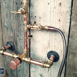 Può includere: Rubinetto doccia in stile industriale con tubi in rame, raccordi in ottone e un tubo metallico flessibile. Montato su una parete in legno invecchiato, il design include una valvola e un soffione. Estetica vintage.
