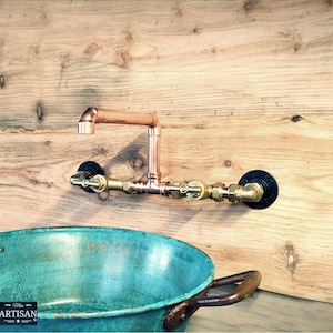 Può includere: Rubinetto e raccordi idraulici in rame montati su una parete di legno, con un lavabo turchese sottostante. Il rubinetto ha un design moderno e industriale. Il lavabo ha un aspetto rustico e invecchiato.