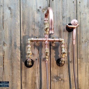 Può includere: Rubinetto doccia in rame con un rubinetto curvo e un soffione separato. L'apparecchio è realizzato con tubi di rame e raccordi in ottone, montato su una parete di legno. Il design ha un'estetica industriale, steampunk.