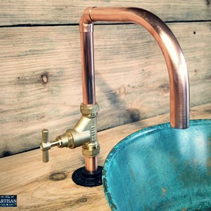 Può includere: Rubinetto per lavabo in tubo di rame con valvola in ottone e becco curvo. Il rubinetto è montato su un piano di lavoro in legno accanto a un lavabo in ceramica turchese.