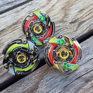 May include: Three colorful spinning tops with intricate designs, featuring green, red, and gold accents. The tops are circular with a central emblem and the text "DZ". They rest on a weathered wooden surface.