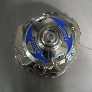 May include: A shiny, silver toy with blue accents and the word "DRIGER" printed on it. The toy has a circular shape with a complex design, featuring multiple layers and textures. The overall appearance is metallic and modern.