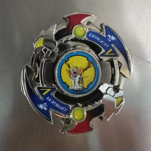 May include: A silver and blue spinning top toy with red and yellow accents. The center features a cartoon image of a white creature with yellow wings. The word "ORIGER" is printed on the blue sections.