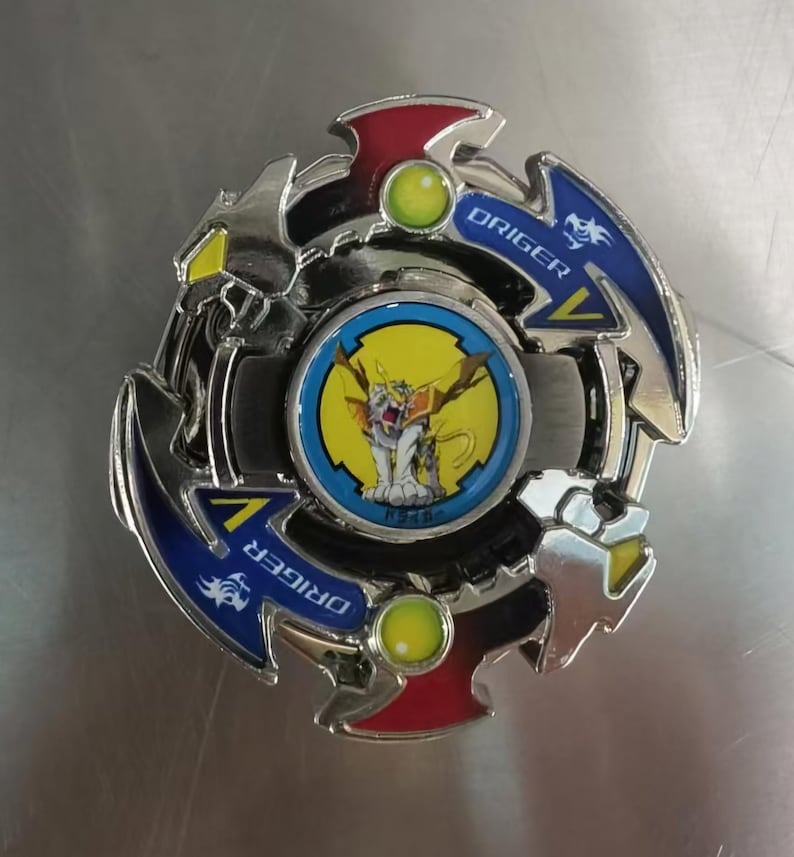 May include: A silver and blue spinning top toy with red and yellow accents. The center features a cartoon image of a white creature with yellow wings. The word "ORIGER" is printed on the blue sections.