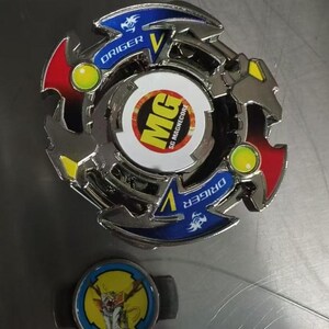 May include: A silver and multi-colored spinning top toy with the text "DRIGER" and "MG SG MAGNECORE". The toy has red, yellow, and blue accents. A smaller, matching piece with a cartoon graphic is also present.