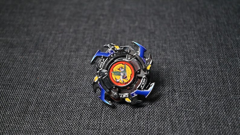 Op de afbeelding: Een zilveren en blauwe Beyblade met een rood en geel centrum. Het centrum heeft een wolfontwerp en de tekst "Wolf" erop.