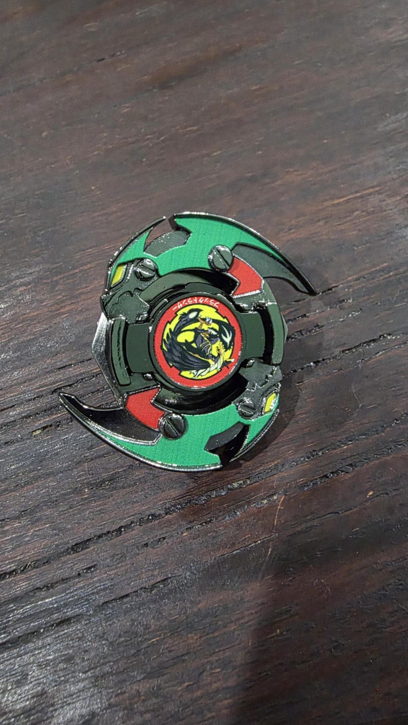 K&ouml;nnte beinhalten: Ein kreisf&ouml;rmiges Kreiselspielzeug mit einem gr&uuml;nen und schwarzen Rahmen mit roten Akzenten. Die Mitte enth&auml;lt ein kreisf&ouml;rmiges Emblem mit einer gelb-schwarzen Drachengrafik, umgeben von einem roten Rand mit japanischem Text in wei&szlig;en Zeichen.