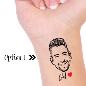 May include: A temporary tattoo featuring a black and white illustration of a man's face with a smiling expression. The tattoo also includes the word "Chad" in cursive handwriting and a red heart.