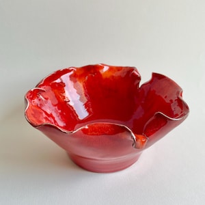 May include: A red ceramic bowl with a wavy, irregular rim. The bowl is glazed with a glossy finish.