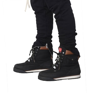May include: A pair of black ankle boots with white soles and laces. The boots have a zipper on the side and a brown leather trim around the top.