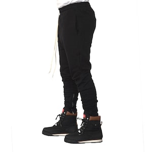 May include: Black sweatpants with a zipper detail on the legs. The sweatpants are worn with black and white boots.