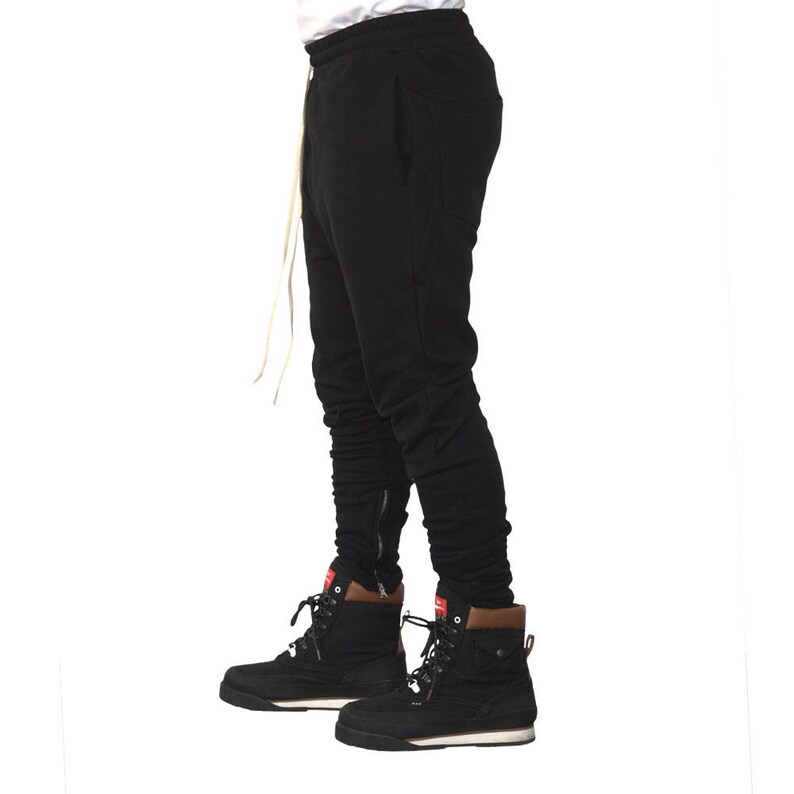 May include: Black sweatpants with a zipper detail on the legs. The sweatpants are worn with black and white boots.