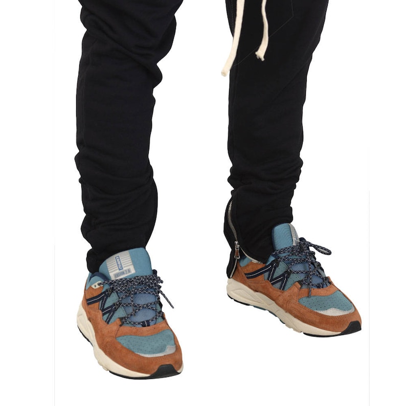 May include: A pair of brown and blue sneakers with a white sole. The sneakers have a blue and black patterned design on the side. The sneakers are being worn by a person wearing black pants.