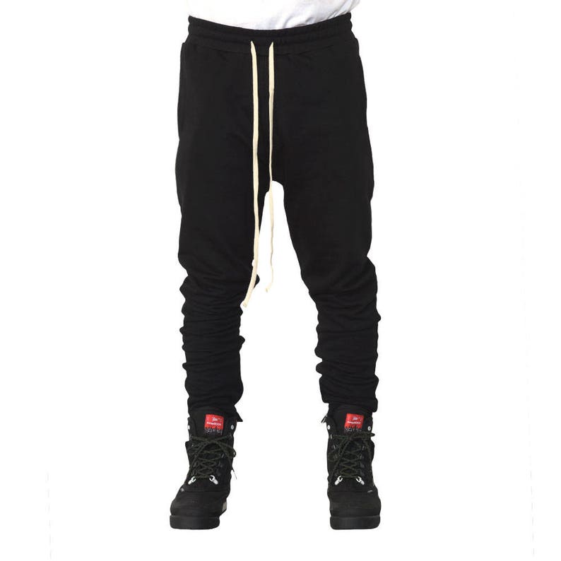 May include: Black sweatpants with a drawstring and a gathered look at the ankles. The sweatpants are worn with black boots.