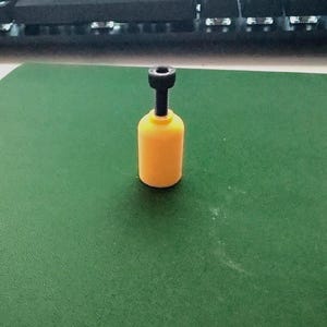 May include: A yellow and black adjustable object with a cylindrical base and a threaded rod. The object is on a green surface, with a keyboard in the background.
