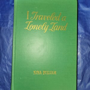May include: A green hardcover book with the title "I Traveled a Lonely Land" in gold lettering. The author's name, "NINA PULLIAM", is also in gold lettering on the front cover.