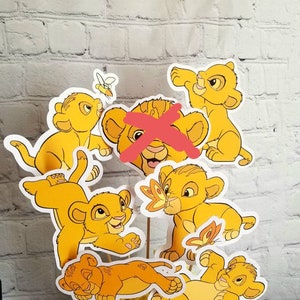 May include: A set of six yellow lion cub character cutouts, perfect for a party centerpiece or decoration. The lion cubs are in various poses, including sleeping, playing, and looking up.