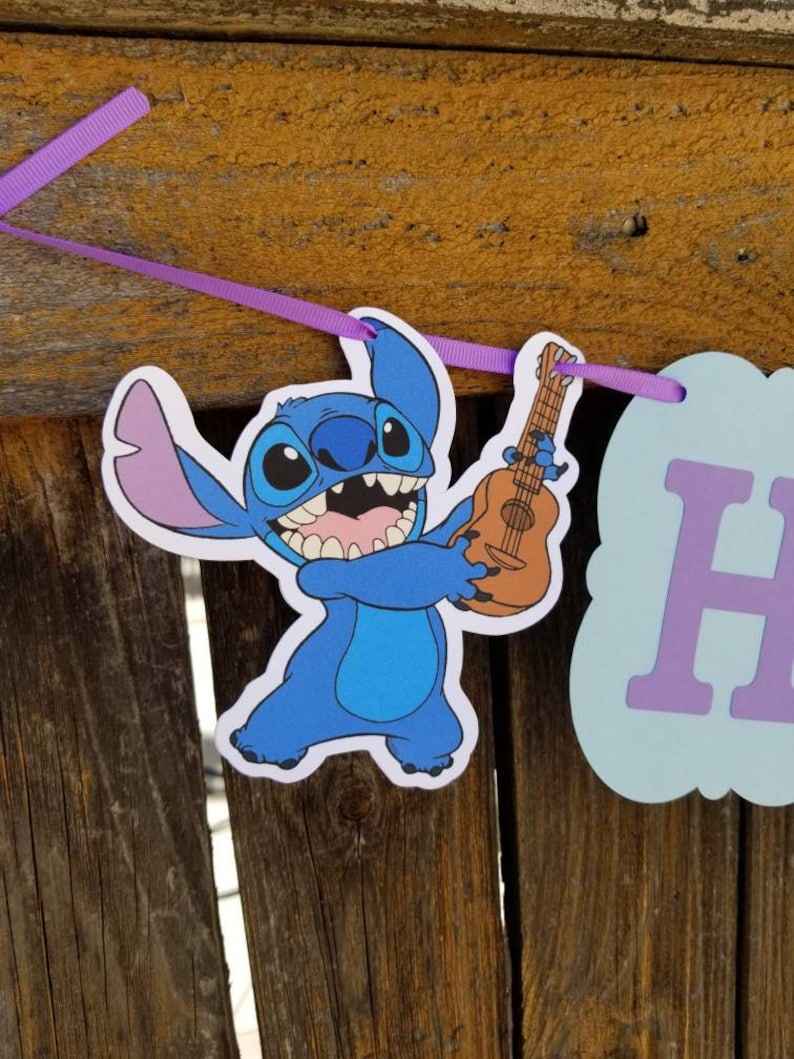 以下が含まれることがあります： ウクレレを持っている漫画のキャラクター、スティッチをフィーチャーしたバナー。キャラクターは青色で、大きな耳と広い笑顔があります。バナーは紫色のリボンでつながれており、水色と紫色の文字が入った看板が含まれています。