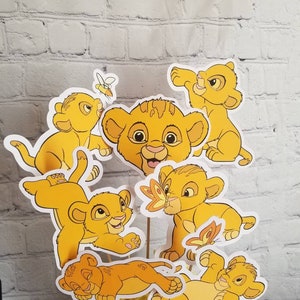 May include: A set of six yellow lion cub centerpieces, featuring different poses and expressions. The lion cubs are all smiling and have black eyes. The centerpieces are perfect for a Lion King themed party.