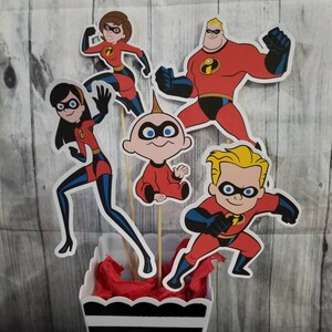 May include: A set of five red and black paper cutouts of the Incredibles family characters. The characters are standing on sticks in a black and white striped container with red tissue paper inside.