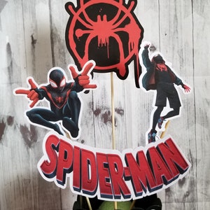 May include: A black and red Spider-Man centrepiece with a black and white polka dot vase. The centrepiece features a red Spider-Man symbol, a red and black Spider-Man character, and a red and black Spider-Man character in a red jacket. The text "SPIDER-MAN" is in red with a blue outline.
