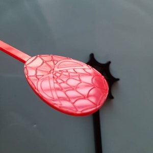 May include: Red plastic spoon with a spider web design. The spoon is part of a set of Spider-Man themed party supplies.