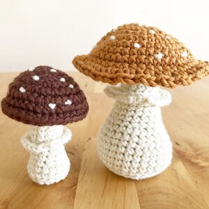 May include: Two crocheted mushroom decorations. One mushroom has a brown cap with white spots and a cream-colored stem. The other mushroom has a tan cap with white spots and a cream-colored stem. Both are handmade.