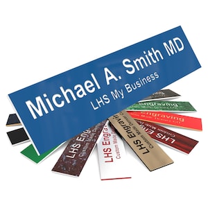 May include: A blue rectangular sign with white text that reads "Michael A. Smith MD LHS My Business". The sign is surrounded by several smaller rectangular signs with different colors and text that reads "LHS Engraving Custom Made Denver CO".