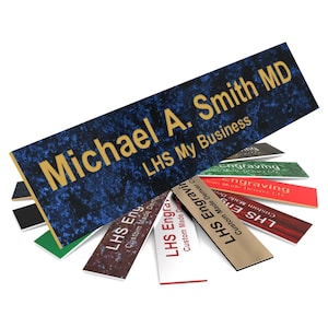 May include: A blue and gold engraved nameplate with the text "Michael A. Smith MD" and "LHS My Business". The nameplate is surrounded by several smaller nameplates with different colors and designs.