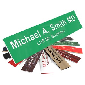 May include: A green rectangular sign with white text that reads "Michael A. Smith MD" and "LHS My Business". The sign is surrounded by smaller rectangular signs with different colors and textures, each with the text "LHS Engraving" and "Custom Made Denver CO".