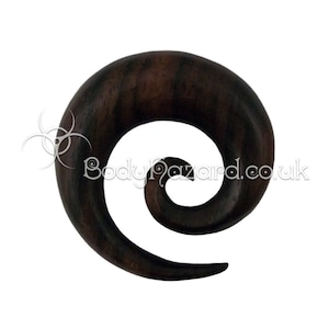 May include: A dark brown wooden spiral ear gauge. The gauge is made of wood and has a spiral design.