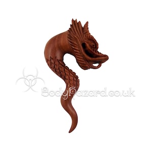 May include: A wooden dragon-shaped ear gauge, carved in a reddish-brown color. The dragon's head is facing forward with its mouth open, and its body is curled into a spiral shape.
