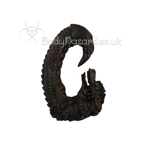 May include: A dark brown wooden dragon ear gauge, carved in a detailed design. The dragon is curled into a C shape, with its head facing the viewer.