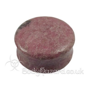 May include: A round, pink and gray stone plug for stretched earlobes. The plug is made of a natural stone with a mottled pattern.