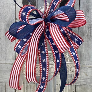 May include: A red, white, and blue ribbon bow with stars and stripes. The bow is tied around a white birdcage.