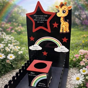 May include: A black memorial with a red star and a giraffe illustration. The memorial has a rainbow and the text "When it rains look for rainbows, When it's dark look for stars." It also includes names and dates.