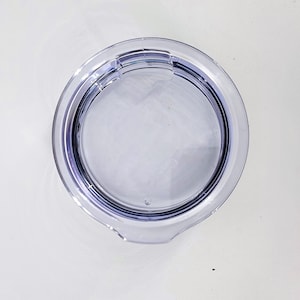 May include: Clear plastic lid for a tumbler or cup. The lid has a lip around the edge and a small hole in the center.