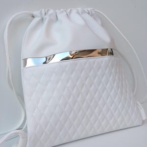 Può includere: Zaino bianco con coulisse, bordino argentato e design trapuntato.