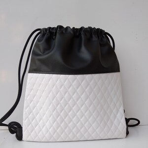 Può includere: Una borsa a cordoncino bianca e nera con un fondo bianco trapuntato e una parte superiore in pelle nera.