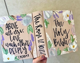 May include: A pink Bible with a floral design and the text "The Holy Bible" and "The Rays 12.10.22". The front cover also has the text "ABOVE all else, LOVE each other DEEPLY 1 PETER 4:8".