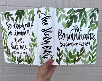 May include: A white Bible with a green leafy design and the text "The Holy Bible" on the spine. The front cover has the text "The Brannans" and "September 2, 2023". The back cover has the text "So they are no longer two, but one. Matthew 19:6".
