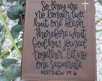 May include: A brown leather-bound book cover with the text "So they are no longer two, but one flesh. Therefore what God has joined together, let no one separate. Matthew 19:6" in black script. A gold cross is in the upper right corner.
