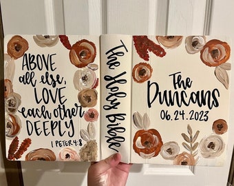May include: A white Bible with a floral design in shades of brown, beige, and white. The text "The Holy Bible" is written on the spine. The front cover has the text "ABOVE all else, LOVE each other DEEPLY 1 PETER 4:8". The back cover has the text "The Duncans 06.24.2023".