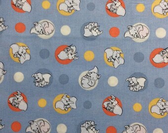 May include: Blue fabric with a repeating pattern of white baby elephants in circles with orange, yellow, and white polka dots. A white measuring tape with black numbers is at the bottom of the image.