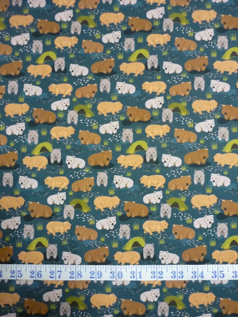 May include: Teal fabric with a repeating pattern of brown and white wombats. The wombats are depicted in a lying down position. The fabric has a white measuring tape with black numbers running across the bottom.
