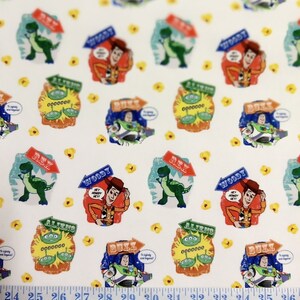 May include: White fabric with a repeating pattern of Toy Story characters, including Woody, Buzz Lightyear, Rex the dinosaur, and the aliens. The characters are in various poses and have speech bubbles with text. The fabric also has yellow flower accents.