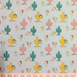 Puede incluir: Una tela azul con un patrón repetido de cactus amarillos, rosas y verdes y un perro de dibujos animados con una gorra de béisbol y una raqueta de tenis. La tela tiene una cinta métrica blanca con los números del 25 al 36 impresos en ella.